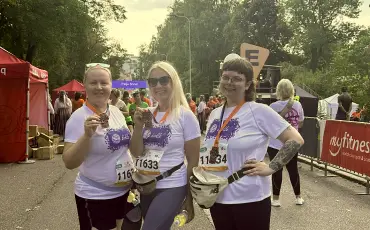 Three people wearing matching purple and white t-shirts at a running event, holding what appear to be participation medals