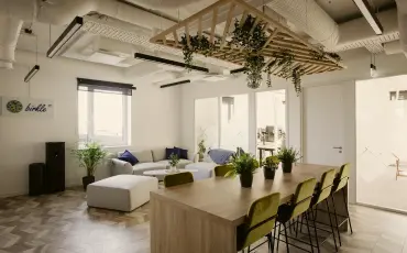 Bright, open-plan office space with white walls, hanging plants, modern furniture including lounge seating and high tables