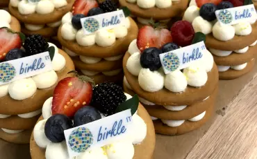 Array of decorated pastries topped with white cream, fresh berries, and small company logo tags