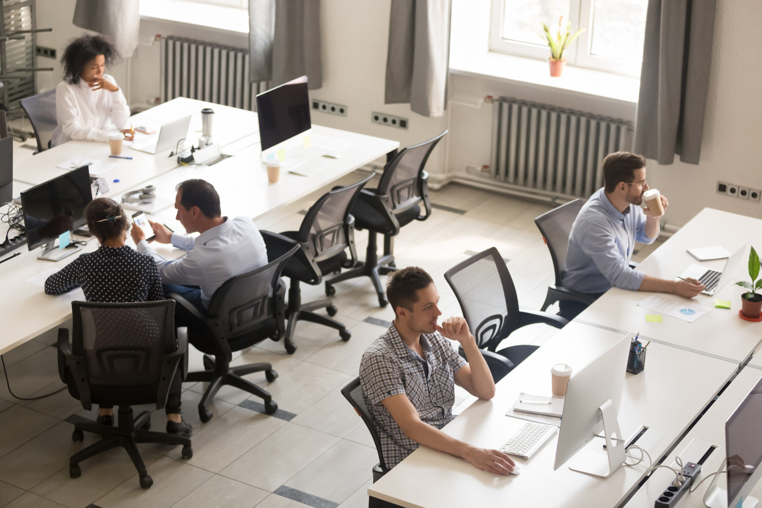 Man in checked shirt working at a computer in a bright modern office with white desks and ergonomic chairs