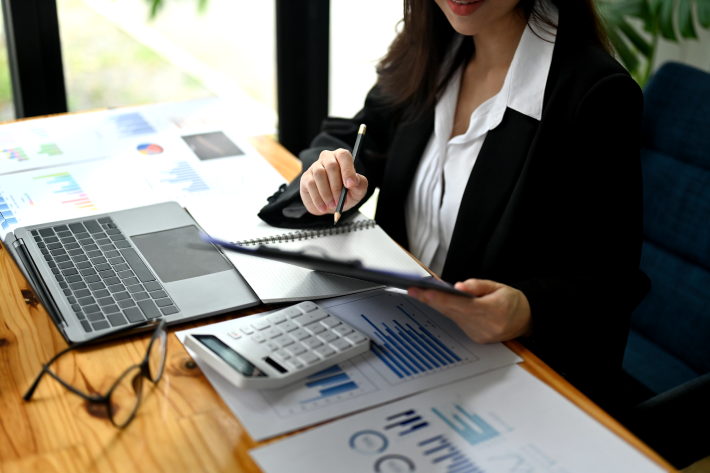 Business person in formal attire reviewing financial charts and graphs while taking notes, with a calculator on the desk