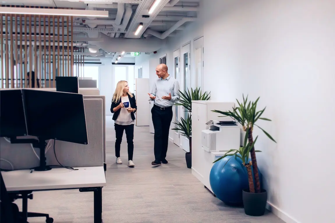 Office workers at their desks with computers in an open workspace environment with black office chairs