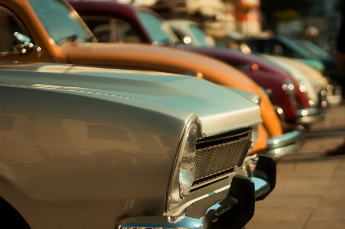 Close-up detail shot of a classic car's front end, showing the headlight and chrome grill in a soft, muted color palett