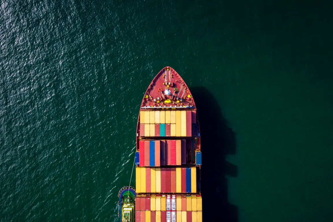 Bird's eye view of a container ship loaded with colorful shipping containers sailing through dark blue waters