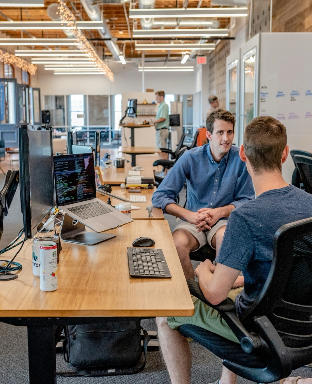 Person working at a desk with multiple monitors in an open office space with exposed ceiling