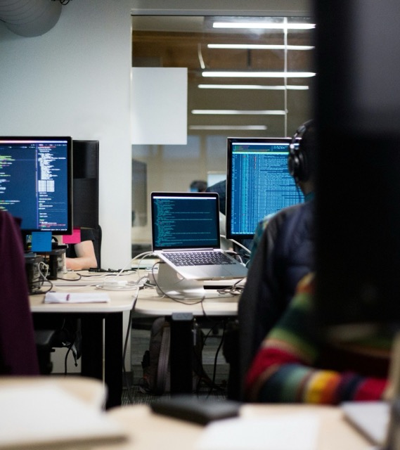 Office workspace with multiple computer monitors displaying data or code in a dimly lit environment