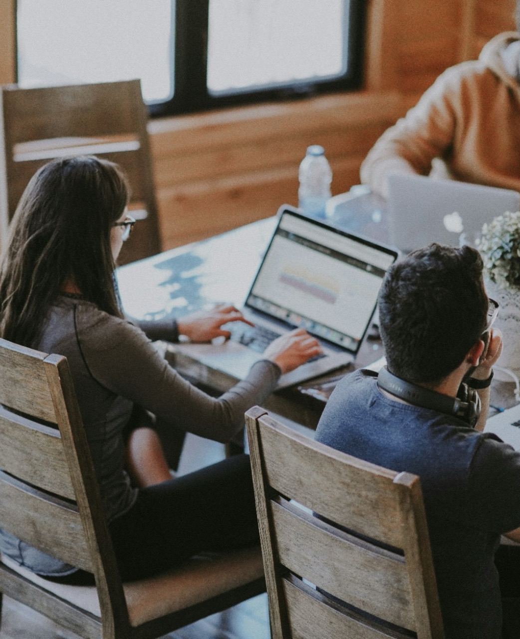 Two people reviewing code on a laptop while sitting together at a wooden table in a collaborative workspace